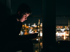 Silhouette einer Person mit Smartphone vor dunklem Hintergrund als Symbol für Suchtverhalten
