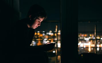 Silhouette einer Person mit Smartphone vor dunklem Hintergrund als Symbol für Suchtverhalten