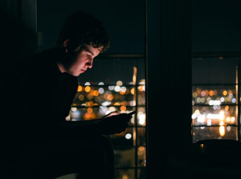 Silhouette einer Person mit Smartphone vor dunklem Hintergrund als Symbol für Suchtverhalten