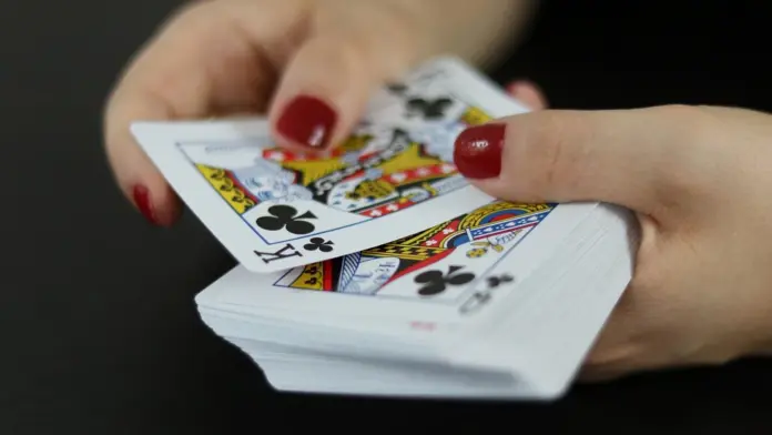 250000-dollar-pgt-championship-2027 Hände mit roten Nägeln halten ein Deck Spielkarten.