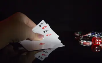 Getrennte Felder, gemeinsames Bracelet: WSOP plant Pro-Am Eine Hand hält vier Asse bei einem Pokerspiel mit Chips und einem Würfel im Hintergrund