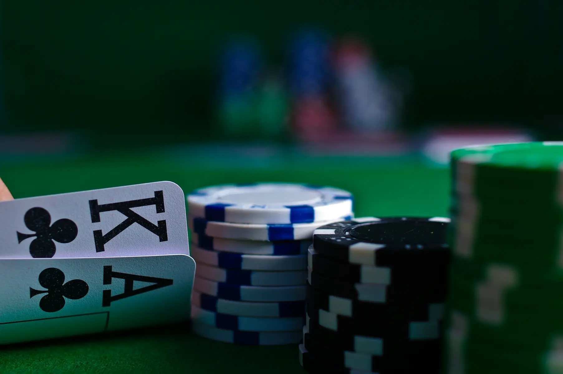 Gestapelte Pokerchips in verschiedenen Farben und zwei Spielkarten auf einem grünen Filztisch